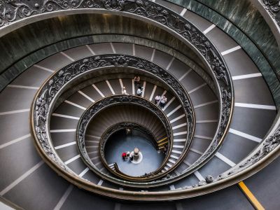 Looking straight down a grand double spiral staircase, with small figures at the bottom.