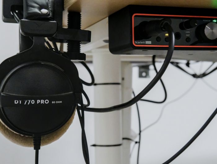 Headphones hanging beside an audio interface and cables under a desk.