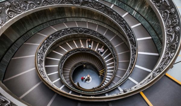 Looking straight down a grand double spiral staircase, with small figures at the bottom.