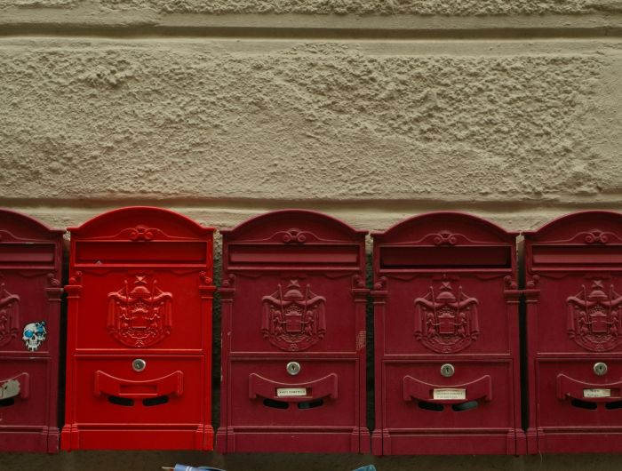 Five red mailboxes in a row on a stucco wall, one of them a brighter red than the rest.