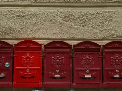 Five red mailboxes in a row on a stucco wall, one of them a brighter red than the rest.