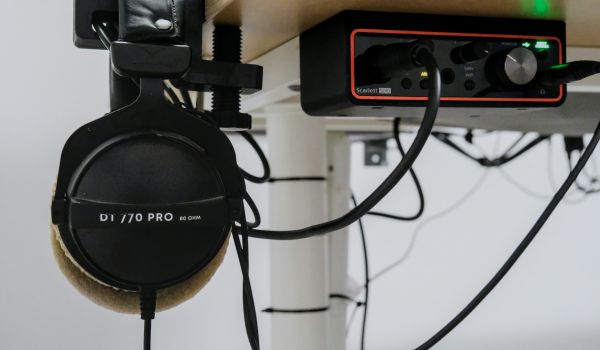 Headphones hanging beside an audio interface and cables under a desk.
