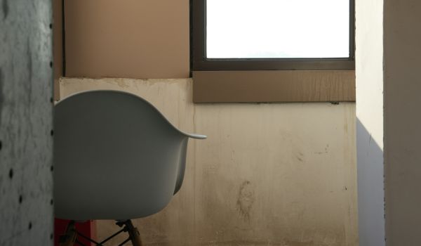 A single empty chair beside a bright window in an otherwise bare room.