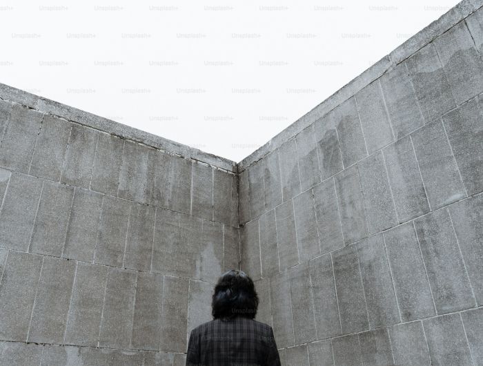 A person standing in the corner of two high concrete walls, seen from behind, looking up.